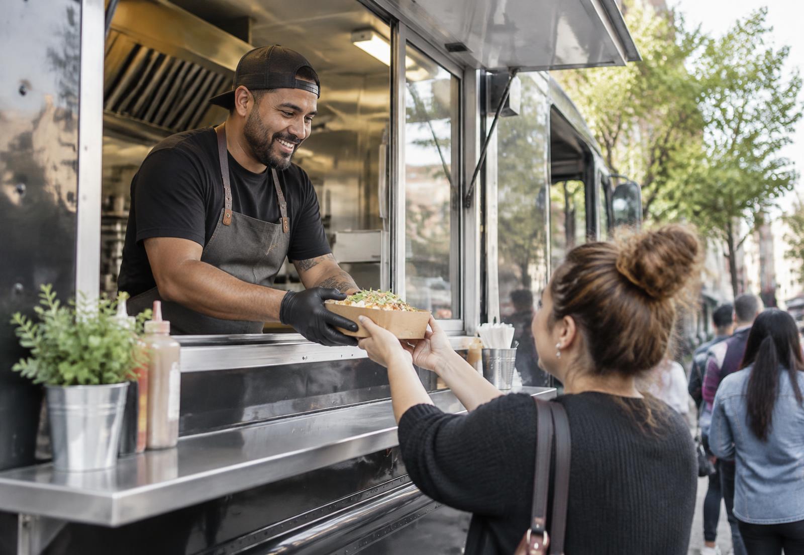 A food truck owner handing an order to a customer at the service window